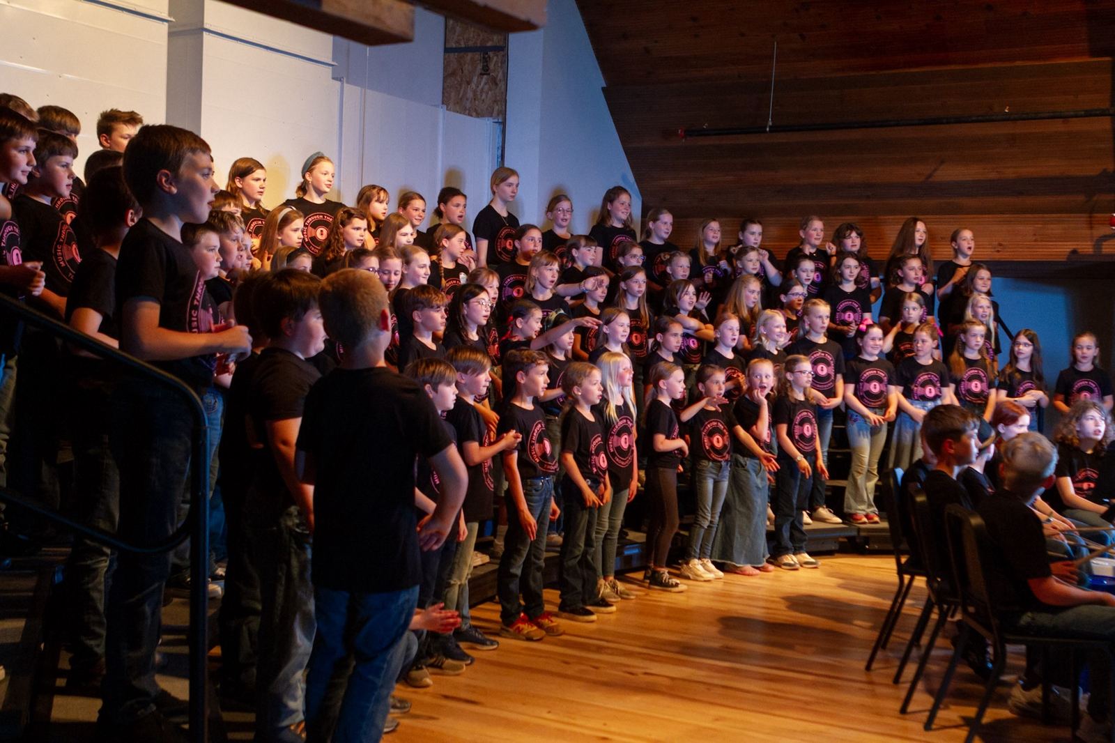 A large children's choir singing in a wood-beamed hall