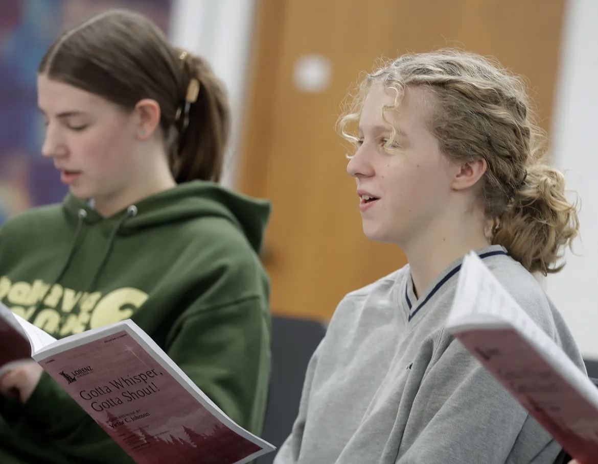 Two students singing from their music in choir rehearsal